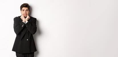 Image of scared and insecure young businessman in suit, trembling from fear and looking horrified, standing over white background photo