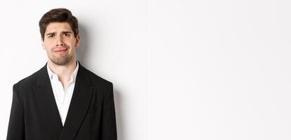 Close-up of confused handsome man in suit, grimacing and looking perplexed, wearing trendy suit, standing against white background photo