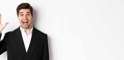 Close-up of handsome businessman in black suit, smiling amazed, showing number five, standing over white background photo