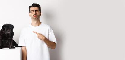 Sad and gloomy pet owner pointing at his black pug dog and sobbing, standing upster against white background photo