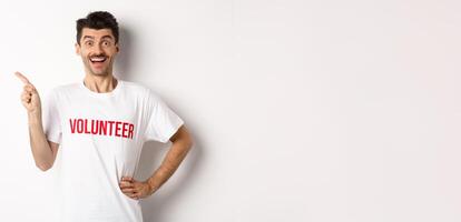 Happy smiling volunteer pointing finger left at copy space, showing announcement, white background photo