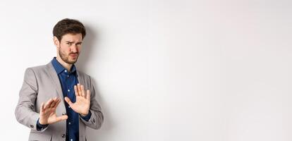 Stay away. Reluctant businessman step back with concerned disgusted face, raising hands to block bad offer, rejecting something awful, telling no and decline proposal, white background photo