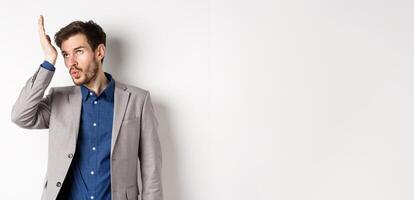 Man shocked with someone very stupid. Annoyed businessman roll eyes and facepalm bothered by crazy clients, standing on white background in suit photo