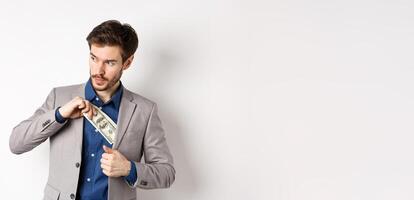 Confident businessman put money in suit and looking aside, standing on white background photo