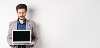 Handsome caucasian businessman in suit showing empty laptop screen, demonstrate promo, standing on white background photo