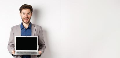 Handsome caucasian businessman in suit showing empty laptop screen, demonstrate promo, standing on white background photo