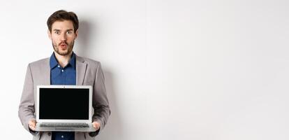 Handsome caucasian businessman in suit showing empty laptop screen, demonstrate promo, standing on white background photo