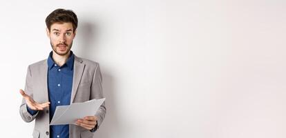 Confused businessman looking at bad document, complaining on deal, pointing at paper frustrated, standing in suit on white background photo