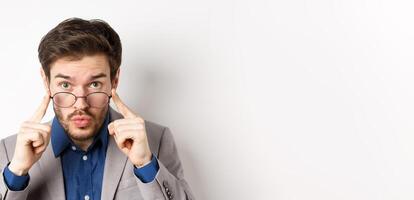 Surprised businessman takes-off glasses and look excited at camera, checking out interesting deal, standing on white background photo