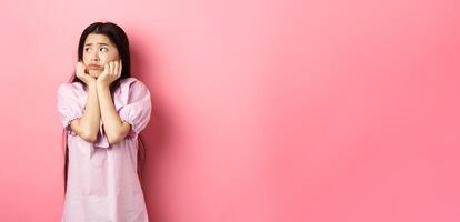 Sad and lonely asian girl look left and frowning, standing distressed against pink background photo
