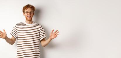 Attractive young man with red hair and glasses showing large size, length of big object, smiling satisfied, standing over white background photo