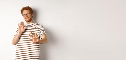 Displeased young man with red hair and bristle showing stop gesture, refusing something bad with disgusted face, standing over white background photo