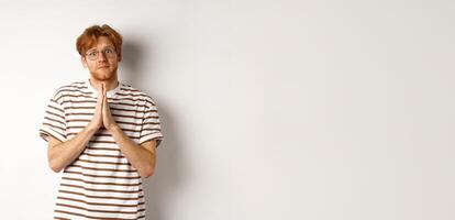 Cute redhead man in glasses asking for help, pleading and looking clingy at camera, begging for favour, white background photo