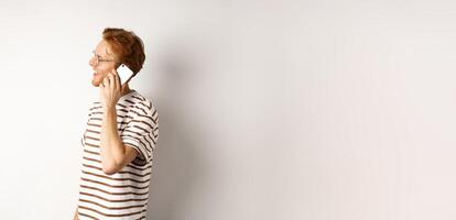 Profile of happy young handsome man talking on mobile phone, looking left and smiling, standing over white background photo