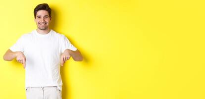 Attractive bearded man pointing fingers down, showing event banner, standing over yellow background photo