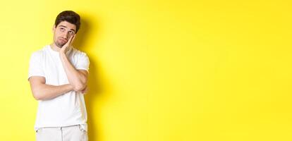 Bored and gloomy guy looking up, imaging things, standing over yellow background photo