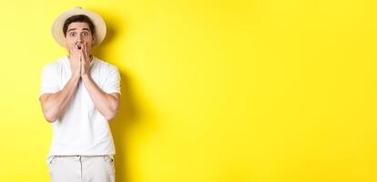Concept of tourism and summer. Shocked guy jumping from fear, standing startled against yellow background photo