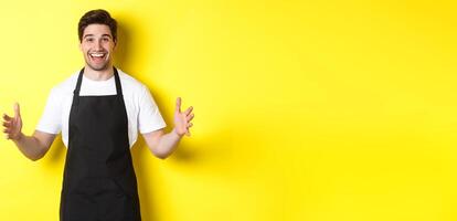 Happy barista holding something big, shaping large object, standing over yellow background photo
