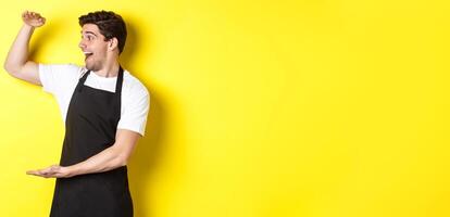 Man looking surprised at something large, standing in black apron against yellow background photo