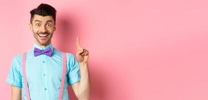 Cheerful caucasian man pitching an idea, raising finger in eureka gesture and smiling, suggesting solution, standing on pink background photo