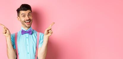 Handsome funny guy pointing fingers aside, showing left and right logo and smiling, recommending two choices, standing on pink background photo