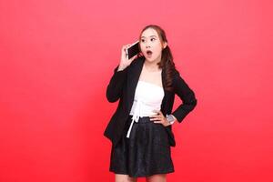 gesture of young asian career woman shocked candid wearing formal black suit while calling someone via smartphone, for technology, business, advertising, financial content photo