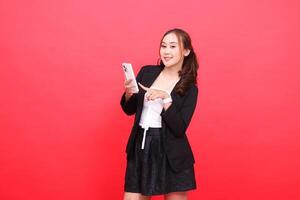 gesture of mature asian career girl smiling at the camera wearing black formal suit hand operating smartphone cellphone while touching it, for technology, business, advertising, financial content photo