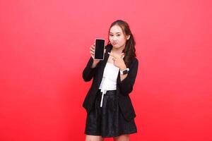gesture of young indonesia career woman frowning wearing a black formal suit holding a smartphone while pointing at it, for technology, business, advertising, financial content photo