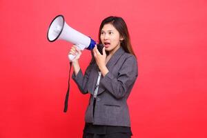 Asian girl manager's expression tilted to the right, screaming in surprise, using a megaphone, holding a candid microphone, wearing a gray jacket and a red skirt. for broadcast and advertising concept photo