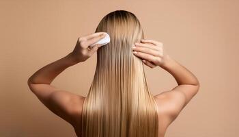 Young woman applying hair mask on beige background, back view photo