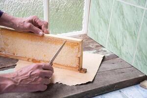 man cuts honeycombs from a honey frame with a knife for eating for tea, honey in honeycombs is good for the health of a pensioner, High quality photo