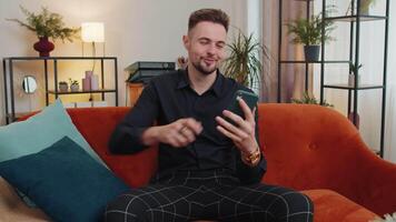 Portrait of adult man sitting on sofa, using smartphone share messages on social media application video