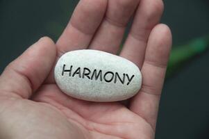 Harmon text engraved on zen stones with hand background. Living a peaceful and harmony life concept photo