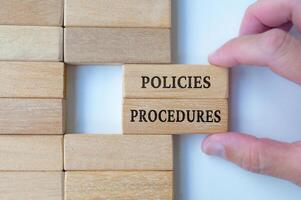 Top view of hand pulling out wooden blocks with text, policies and procedures photo
