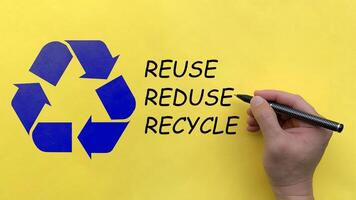 Hand writing reuse, reduce and recycle text on yellow background with recycle symbol. Recycle concept photo