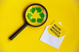 Top view of magnifying glass with recycle symbol and reuse, reduce and recycle text on paper envelope. photo
