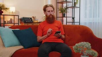 Portrait of adult man sitting on sofa, using smartphone share messages on social media application video