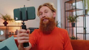 Bearded man blogge taking selfie on smartphone communicating call home online with subscribers video