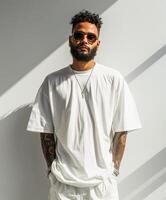 Man with beard and tattoos standing in front of white wall photo