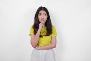Thoughtful young Asian woman in a yellow shirt and white skirt is looking down and appears to be thinking. Concept of introspection and contemplation. photo