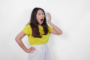 Tired Asian woman in a yellow shirt and white skirt is making a face and yawning feeling sleepy. Concept of boredom or disinterest. photo