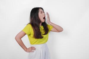 Tired Asian woman in a yellow shirt and white skirt is making a face and yawning feeling sleepy. Concept of boredom or disinterest. photo