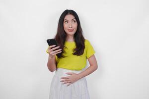 Hungry Asian woman is holding a cell phone and looking to the copy space upwards, thinking what to eat, isolated by white background. photo
