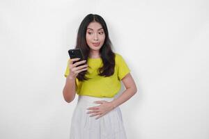 Hungry Asian woman is holding a cell phone and looking to the copy space upwards, thinking what to eat, isolated by white background. photo