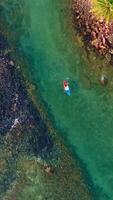 Aerial drone view of kayaking boat over coral reef around rocky coastline with clear turquoise sea video