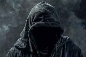 Man in a hood, a shadow hides his face on dark background. Anonymous crime concept photo