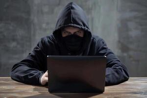 Hacker in hood hacking at computer in dark room. Computer criminal uses malware to hack devices photo