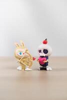 Labubu and Tycoco the monsters mischief diary, Two whimsical figures, a rabbit with a bow and a skull-headed figure holding an apple, engage in a playful interaction. photo