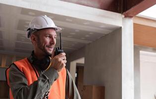 Young Engineer Communicating on Construction Site with Walkie-Talkie, Wearing Safety Gear and Helmet, Overseeing Modern Building Project photo