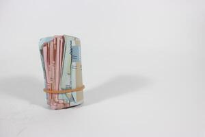A packet of several rupiah bills is folded in half and tied with a rubber band. Bundle isolated on white background with clipping path. photo